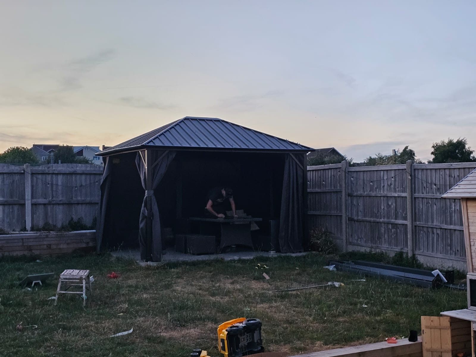 Completed hard-top garden gazebo with curtains at dusk — Newport garden build